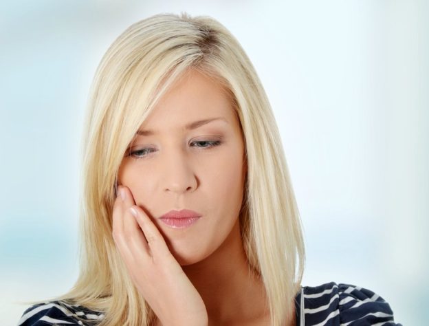 woman holding her jaw in pain prior to receiving TMJ treatment in Indiana